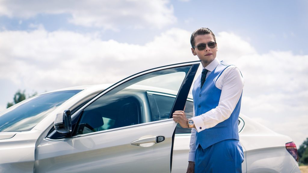 A well-dressed man steps confidently out of a luxury white car under a bright sky—capturing the professionalism and efficiency that business fleet owners gain through smart Montana LLC vehicle registration solutions.