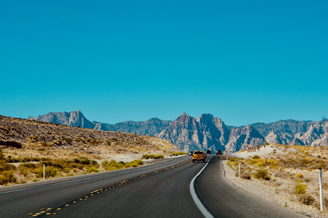 A car cruises down a desert highway with rugged mountains ahead—perfect timing for a Montana car title transfer.