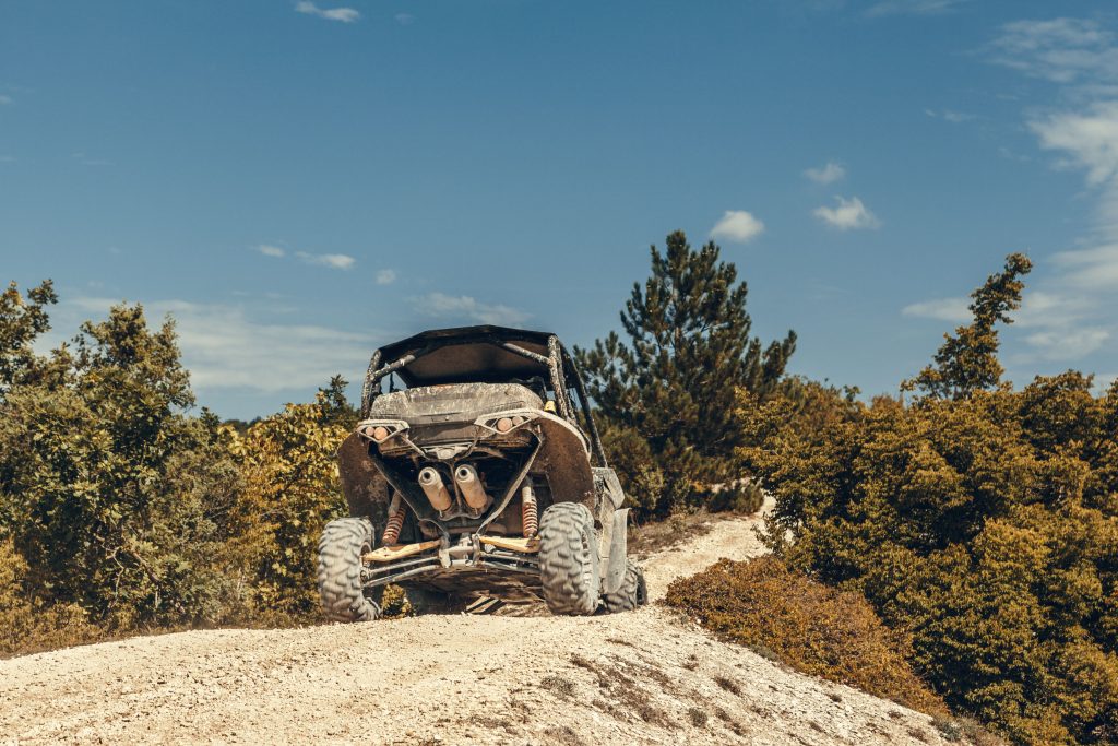 Off-road side-by-side vehicle climbing a sandy trail surrounded by dense brush and trees