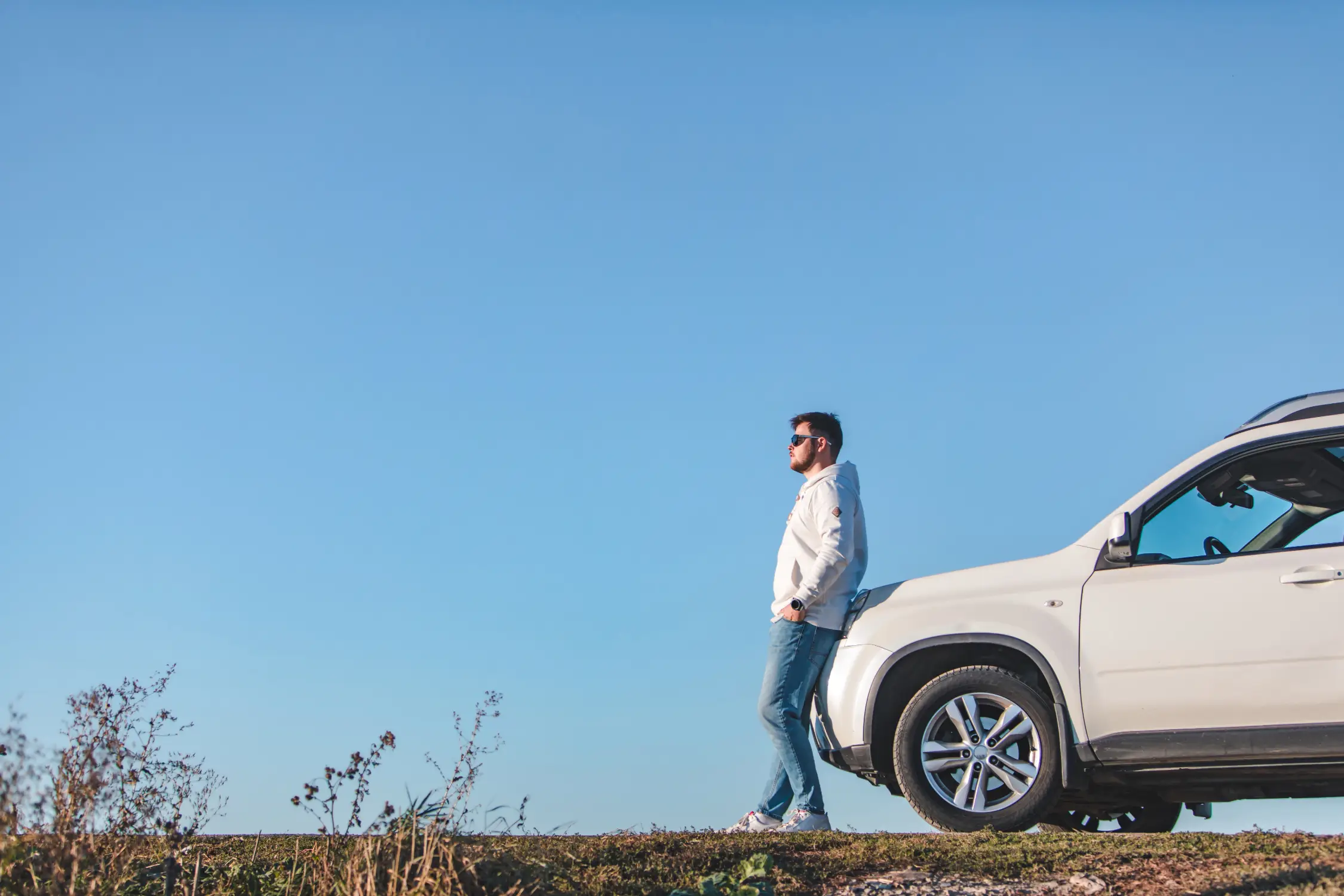 Montana LLC Vehicle Registration & Formation Services - Montana Registration Services A man stands beside his white SUV under a clear blue sky, representing Montana LLC vehicle registration and formation services for out-of-state vehicle owners.
