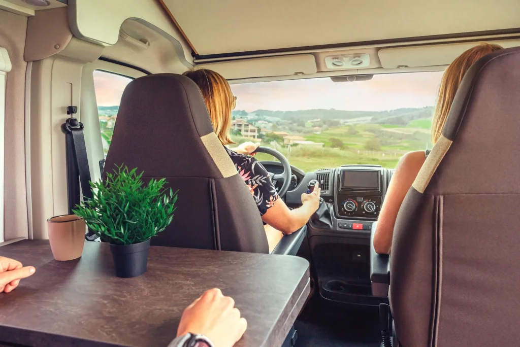 RV driving along a scenic mountain road surrounded by pine forests and wildflowers, representing travel freedom with a Montana LLC RV registration.