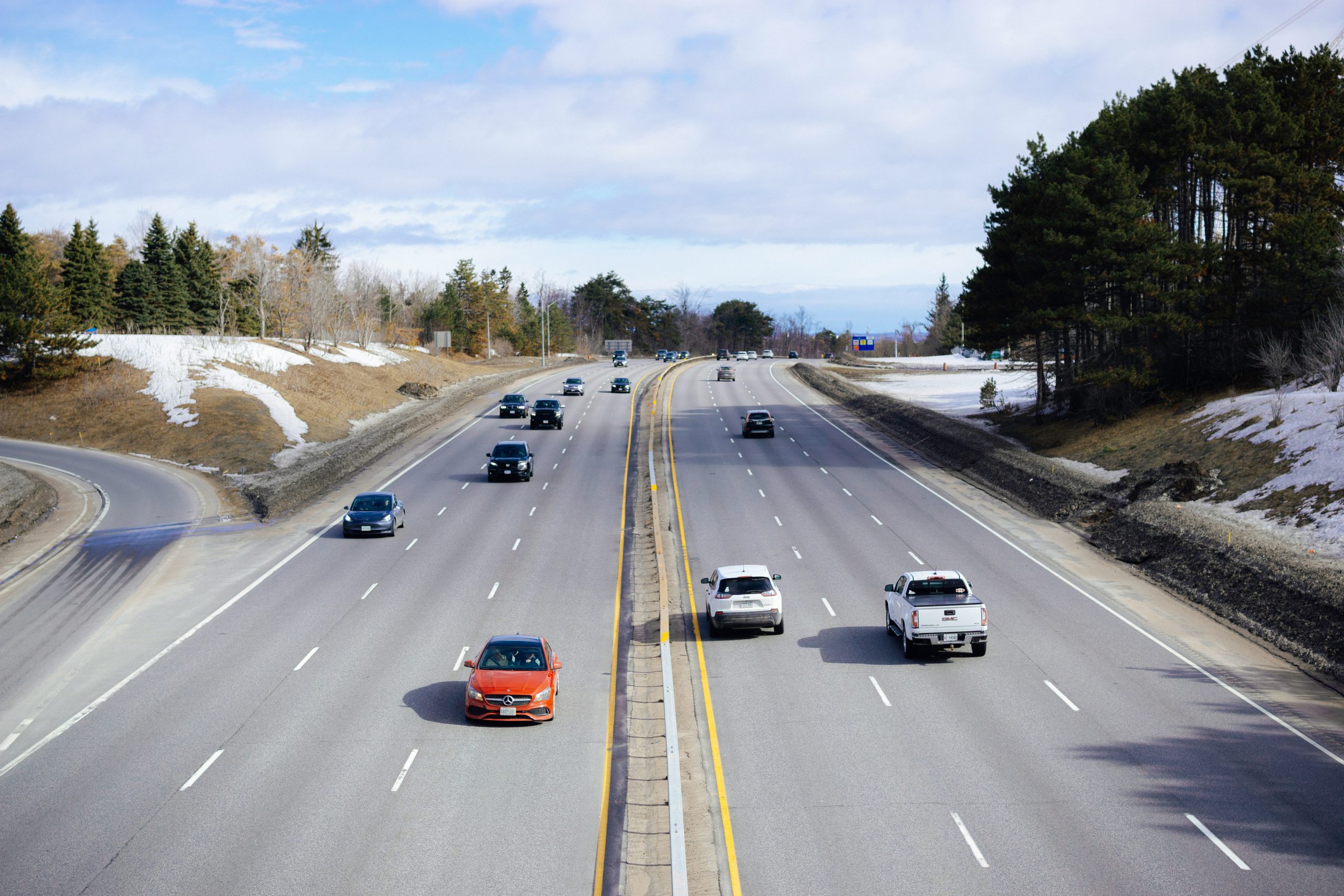Highway traffic on a multi-lane road with cars and trucks traveling through a lightly wooded area with patches of snow, illustrating vehicle usage relevant to an LLC in Montana