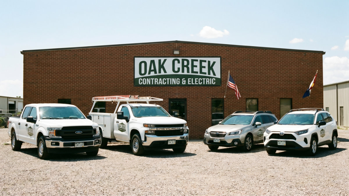A branded fleet of white service trucks and SUVs for "Oak Creek Contracting & Electric" lined up outside their brick business headquarters, representing the localized and specific needs of small to mid-sized fleet vehicle registration and asset tracking.